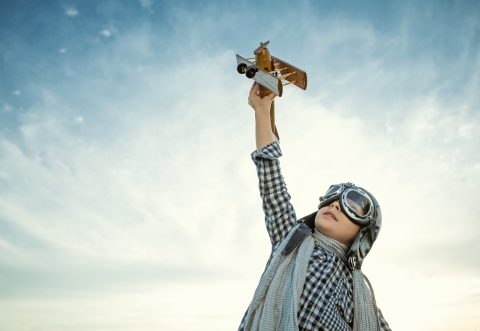 child with aviator helmet flying a toy plane